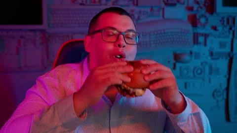 The Fat gamer plays at the computer and eats a burger and pizza. A Thick program Stock Footage 220424357