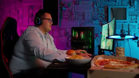 The Fat gamer plays at the computer and eats a burger and pizza. A Thick program Stock Footage 220546355