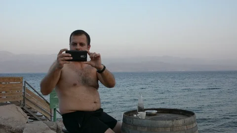 A fat handsome man drinking hot coffee outside near the sea enjoying this moment 動画素材 97100255