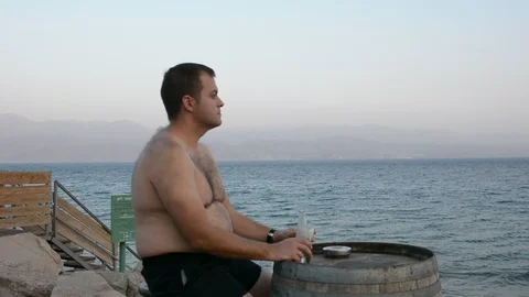 A fat handsome man drinking hot coffee outside near the sea enjoying this moment 스톡 동영상 97100521