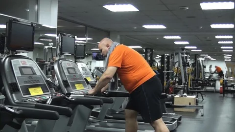 Fat handsome man is very tired going on treadmill Stock Footage