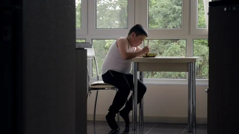 Fat little boy sits in kitchen at table, eats soup Stock Footage 87822844