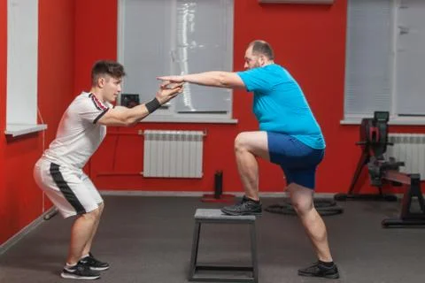 Fat man is diligently doing step-up exercise under control of a personal Stock Photos