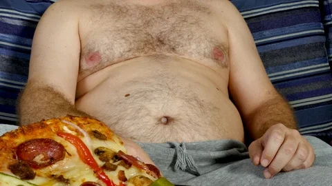 Fat man eating pizza and using TV remote on couch, unhealthy lifestyle concep Stock Footage 104867207