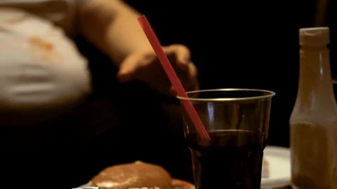 Fat man eats junk food and drinks soda, watches TV at home. Gluttony and Stockbeeldmateriaal 130102414