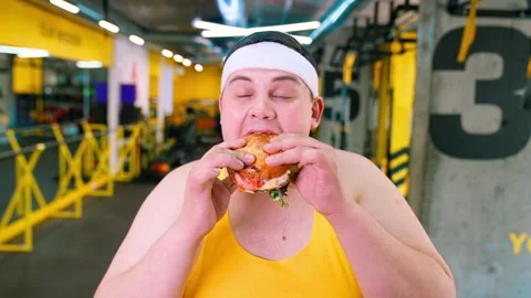 The fat man is exercising in the gym and looking at the burger and pizza. Obesit Stock Footage 244237178