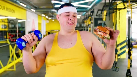 The fat man is exercising in the gym and looking at the burger and pizza. Obesit Stock Footage 244237475