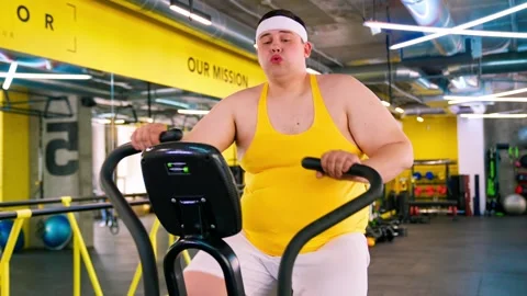 The fat man is exercising in the gym and looking at the burger and pizza. Obesit Stock Footage 244239194