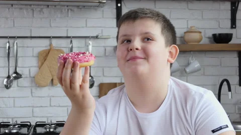 The fat man happily eats a donut in the kitchen. Chubby teen eats a donut Stock Footage 233121522