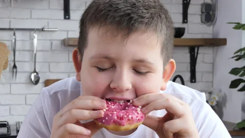 The fat man happily eats a donut in the kitchen. Chubby teen eats a donut Stock Footage 233608893