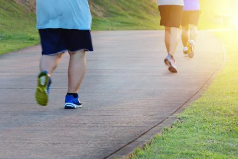 Fat man jogging, catching up with thin men. Low angle view of runners running Stock Photos