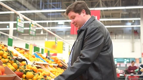 Fat man picking out fruit, oranges in supermarket Stock Footage 84139601