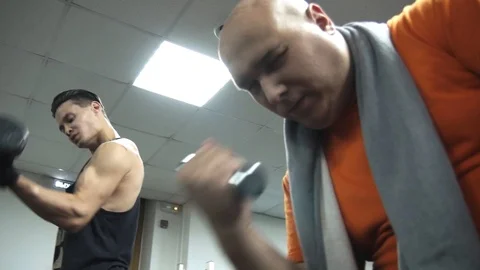 Fat man is picking the smallest dumbbells, near him young handsome ethlete 스톡 동영상 96818255