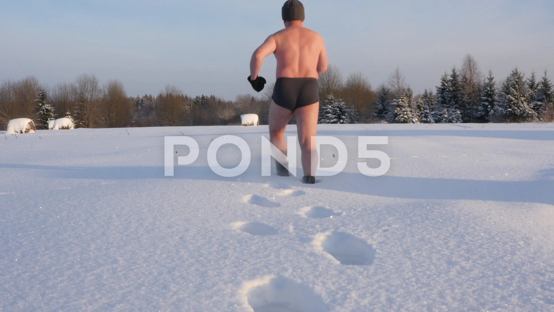 Fat man stripped to his underpants walks across a snowy field