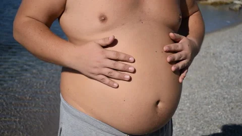 Fat man stroking his belly standing on the ocean. Overweight and health problem 動画素材 96489337