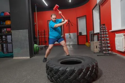 Fat man is very persistent training with sledgehammer and tire in the gym Stock Photos