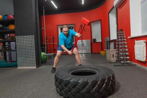 Fat man is very persistent training with sledgehammer and tire in the gym Stock Photos