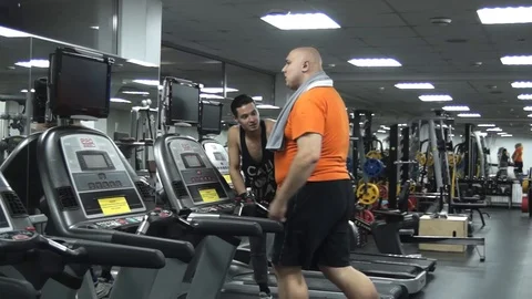 Fat man walking on the treadmill. Man's handsome young coach approves 스톡 동영상 96669893