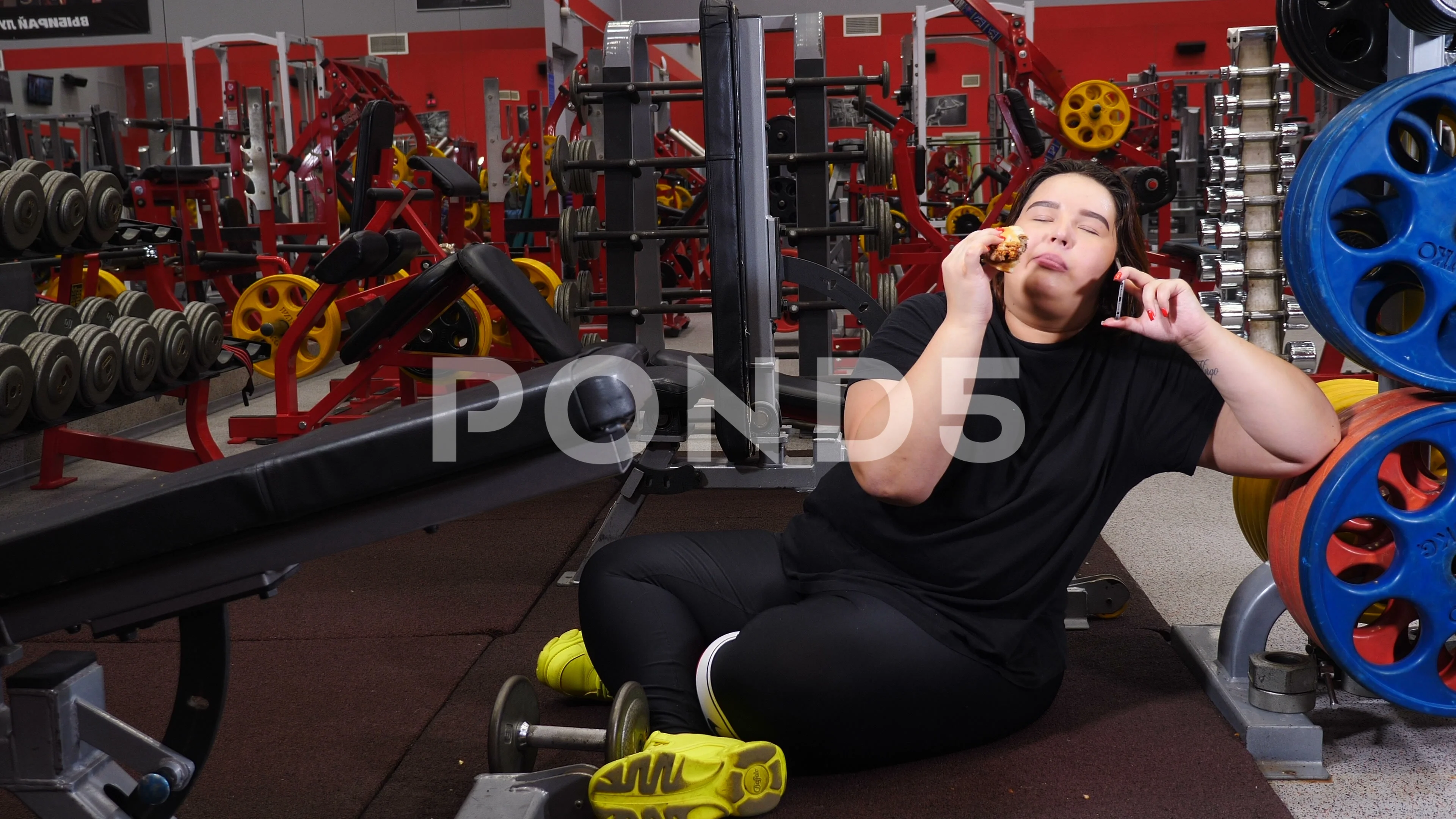 Fat woman and burger in gym. Willpower concept. Obese young pleasant woman