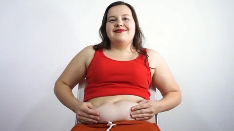 Fat young woman sitting on a chair and touches the fat on stomach. Smiling Stock Footage