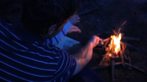 Father adding paper to a small campfire Stock Footage 44446701