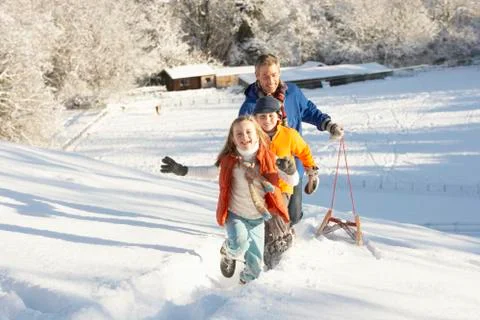 Father and children pulling sledge up snowy hill Stock Photos