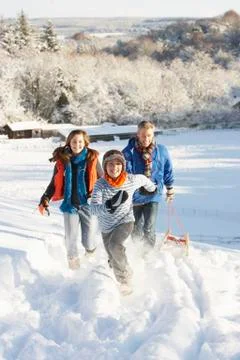 Father and children pulling sledge up snowy hill Foto stock