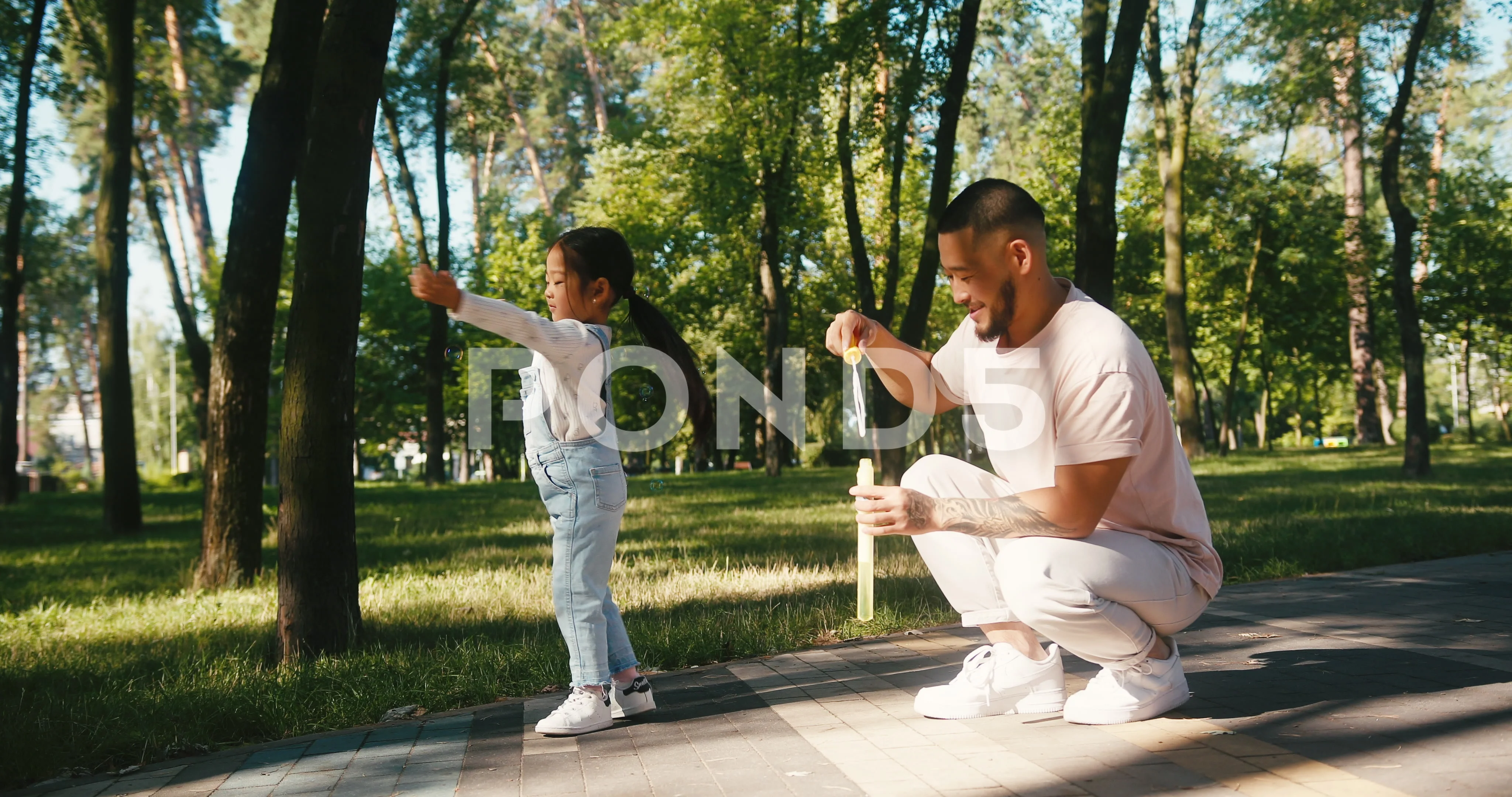 Father and daughter play blowing bubbles in morning park