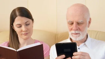 Father and daughter reading e-book and physical print book. Concept of paper vs Stock Footage 85860170