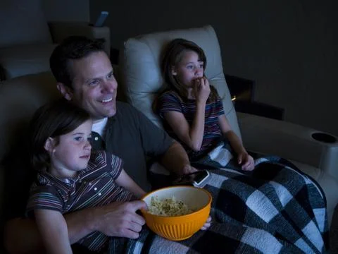 Father and daughters watching movie in home theater Stock Photos