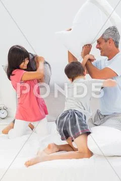 Father and his children fighting together with pillows on bed Stock Photos