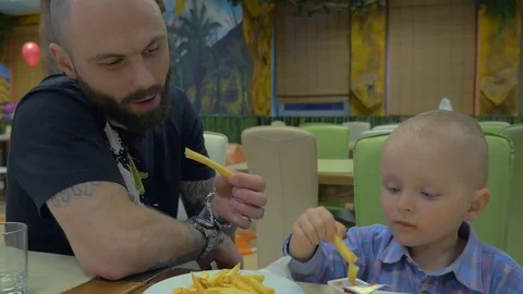 Father and his little son eating french fries together in Cafe Stock Footage