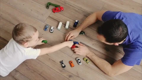 Father and little son lie on warm wooden floor of house and play in toy cars Stock Footage