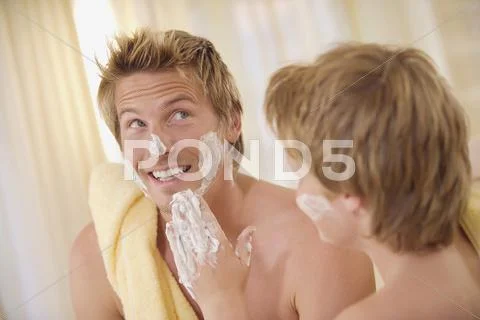 Father and son (10-11) with shaving foam on faces in bathroom Stock Photos