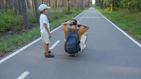 Father and son are learning to skateboard. A boy pushes a man with a backpack on Video stock 205528020