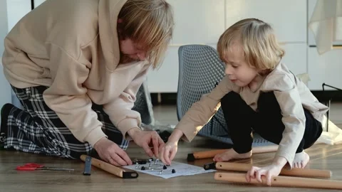 Father and son assembling a chair according to instructions on the floor Stock Footage 305946938