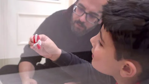 Father and son assembling sugar cane decoration on home glass door for christmas Stock Footage 345253188