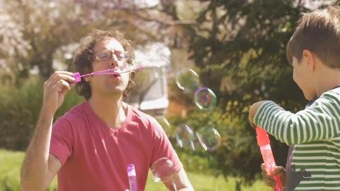 Father and son blowing bubbles together outside in slow motion Stock Footage 80012721