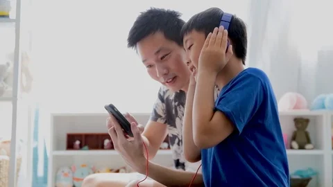 Father and son in blue headphones is using a smartphone Stock Footage 96373553