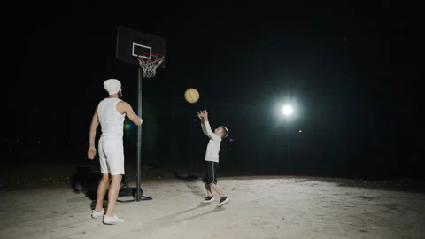 Father and son bonding over basketball practice outdoors at night in slow motion Video stock 302822441