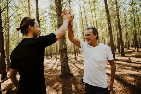 Father and son bonding while exercising in the forest together, high five Stock Photos