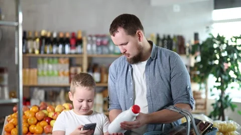 Father and son boy in store scans QR code on milk bottle. With help of mobile Stock Footage 313876388