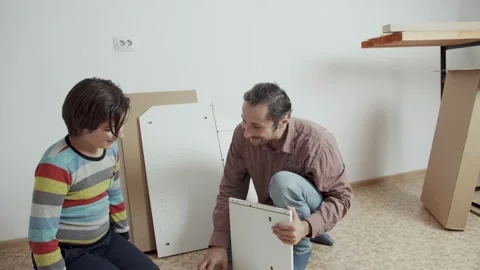 Father and son communicate cheerfully and assemble furniture according to the in Stock Footage 171719337