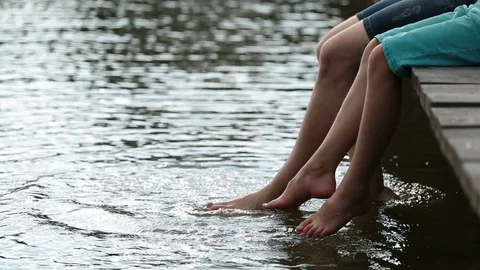 Father and son dangling legs into water and splash Stock Footage 78573271