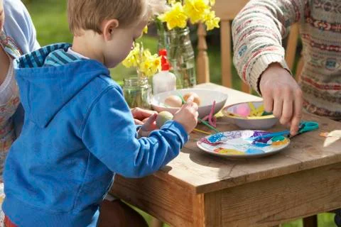 Father and son decorating easter eggs on table outdoors Stock Photos