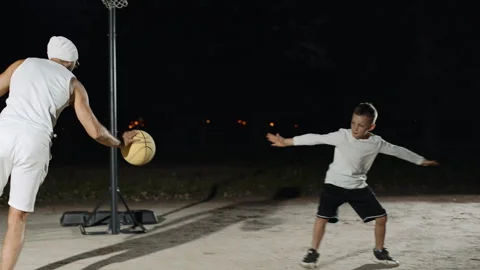Father and son enjoy a friendly basketball game at night in the park Video stock 284212864