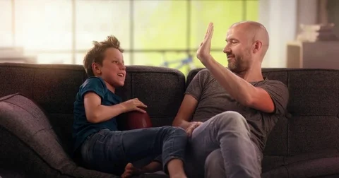 Father and son fail to do high five on the couch Video stock 78663196