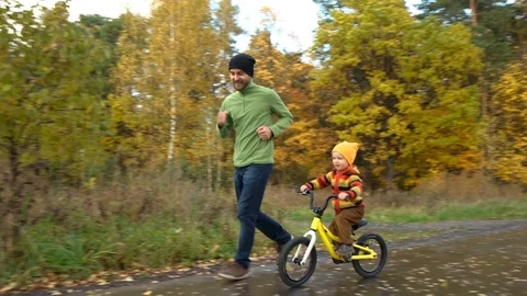 Father and son have fun in autumn park. Cute toddler boy practicing cycling Stock Footage 118268768
