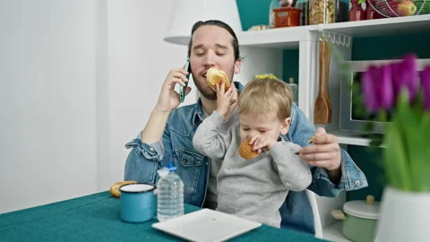 Father and son having breakfast talking on smartphone at dinning room Stock Footage 237293468