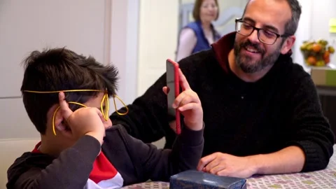 Father and son having fun with Christmas gift ribbons at home Vídeo Stock 345253252